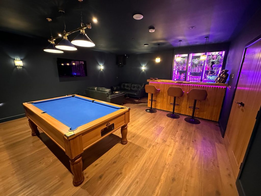 Stylish home entertainment room with a wooden bar, pool table, leather seating, and modern lighting.