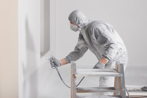 Professional spray painter in protective gear applying paint to a wall with a spray gun.